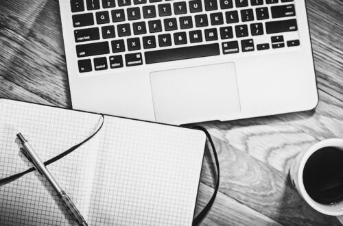a laptop and notebook and a cup of coffee in black and white